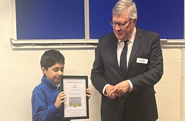Roger Hirst MBE awards certificate to young pupil for designing clear, hold, build logo
