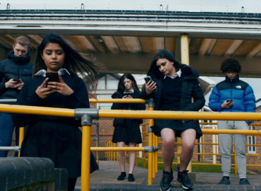 Five teenagers sitting on railings looking at their mobile phones.