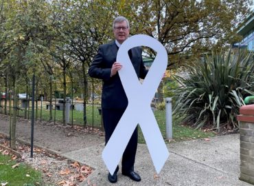 Photo of Roger Hirst holding a giant white ribbon.