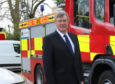 Roger Hirst standing in front of a police car and a fire engine.