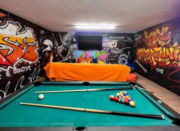 A pool table in a room at The Base Project. There is street style themed artwork on the walls.