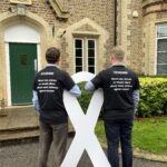 Greg and Darren standing with a White Ribbon logo board wearing the T-shirts