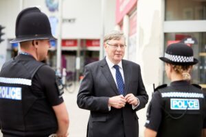 PFCC Roger Hirst standing in front of two police officers in their uniforms in Chelmsford Town Centre.