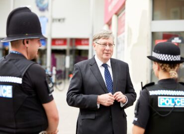 PFCC Roger Hirst standing in front of two police officers in their uniforms in Chelmsford Town Centre.