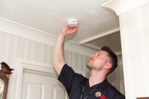 A fire service worker is fitting a smoke alarm onto a ceiling. 