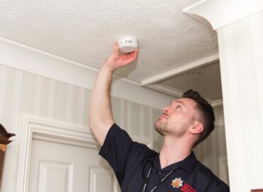 A fire service worker is fitting a smoke alarm onto a ceiling.