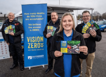 Four people standing in front of a blue banner which says Vision Zero. They are smiling and holding leaflets about road safety.