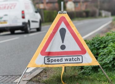 A speedwatch hazard sign shaped like a triangle in the road.